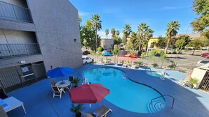 A swimming pool with lounge chairs and umbrellas, surrounded by palm trees and a parking lot. - Motel 6 Sacramento, CA - Natomas & SMF Airport (Sacramento)