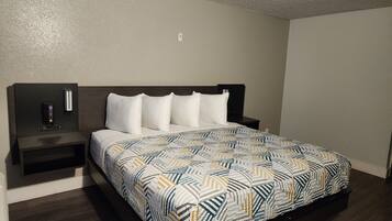 A hotel room with a bed, a nightstand, a phone, and a wall socket.