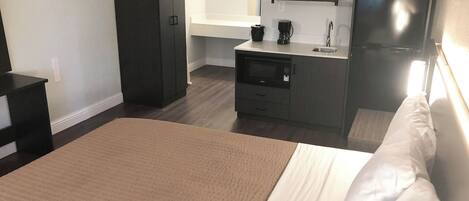 Ein Hotelzimmer mit Bett, Schreibtisch, Kleiderschrank, Mikrowelle, Kaffeemaschine und Kühlschrank.