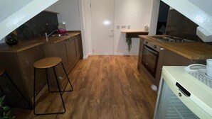 A compact kitchen with wooden flooring, a white door, and a small countertop.