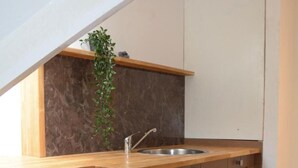 A compact kitchen with a wooden countertop, a single bar stool, a built-in sink, and a dark backsplash.