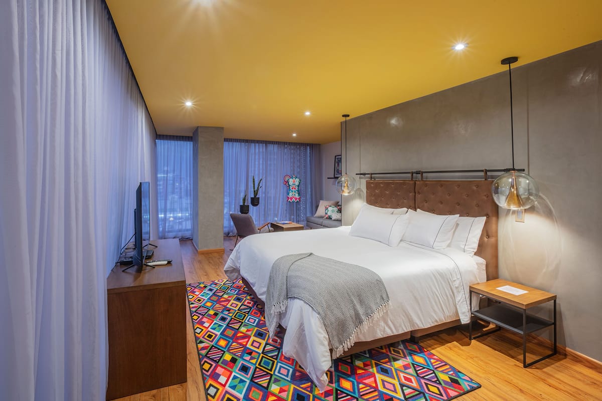 Une chambre moderne avec un grand lit, une table de chevet, une télévision et un tapis coloré.