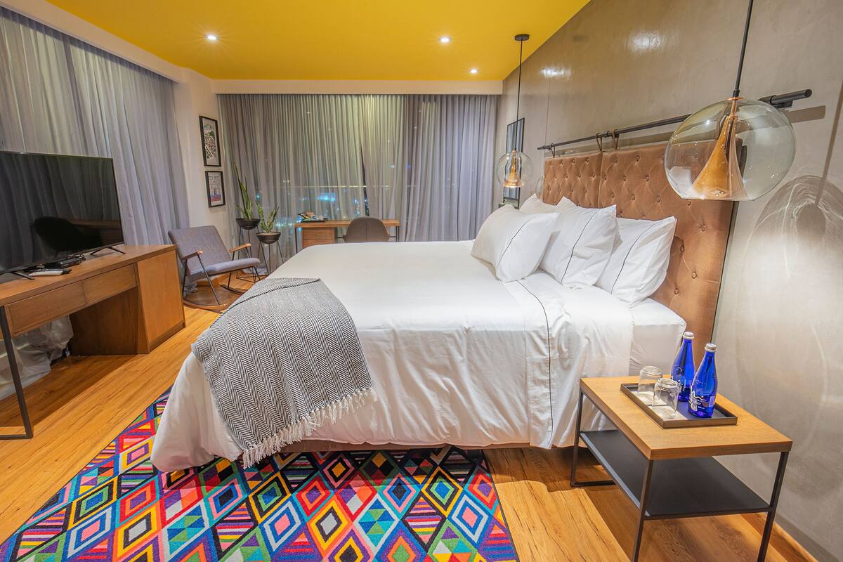 Une chambre d’hôtel moderne dotée d’un grand lit, d’un bureau, d’une télévision et offrant une vue sur la ville.