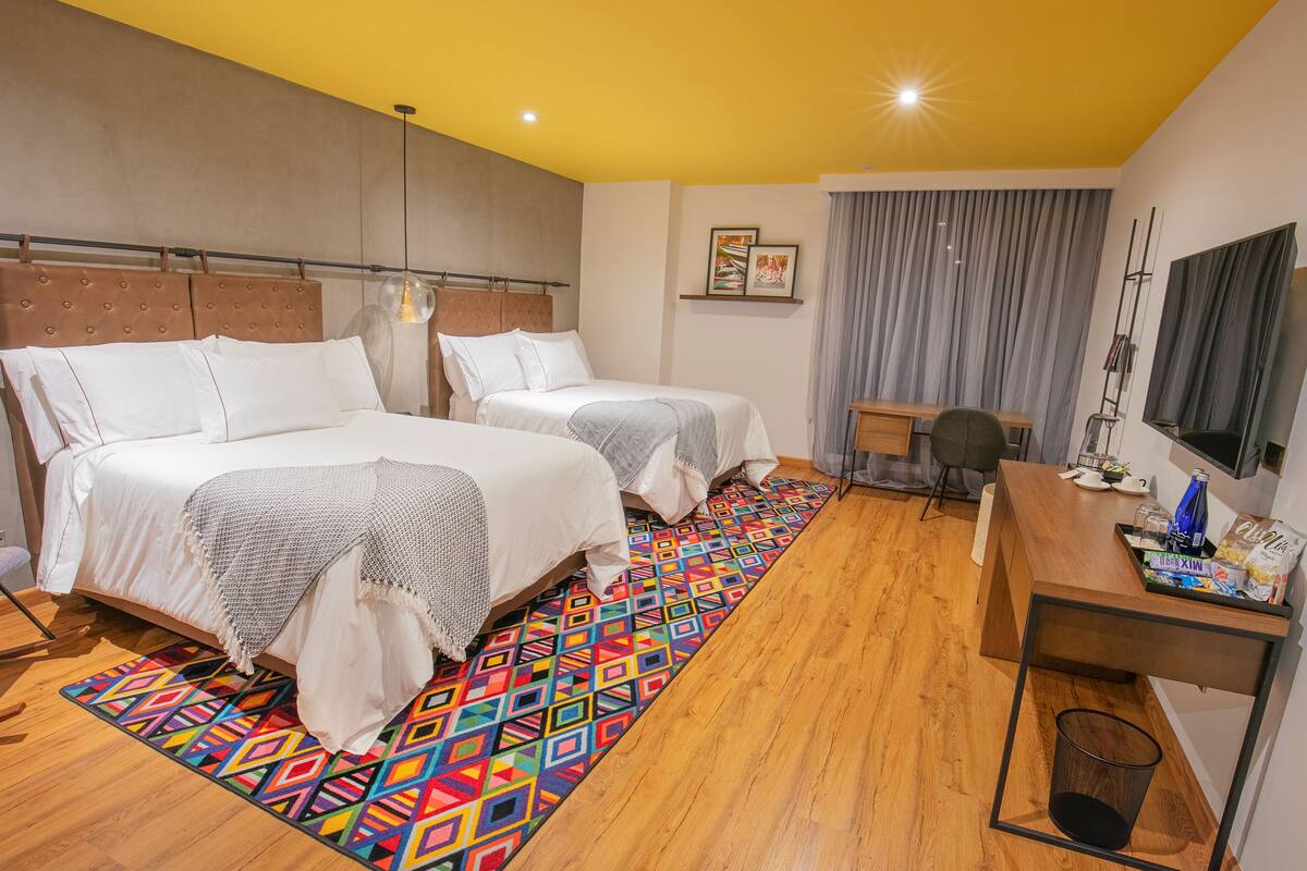 Une chambre d’hôtel avec deux lits, un bureau, une télévision et un tapis aux couleurs vives.
