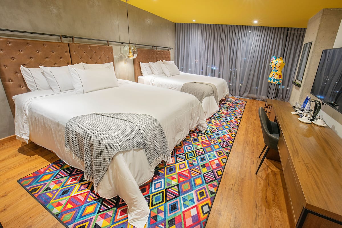 Une chambre d’hôtel avec deux lits, un bureau en bois et un tapis aux couleurs vives.