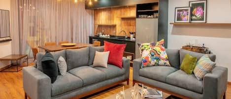 A modern living room with two grey sofas, a wooden coffee table, and a dining area with a table and chairs.