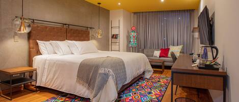 A modern hotel room with a large bed, a desk, a chair, a TV, and a colorful rug.