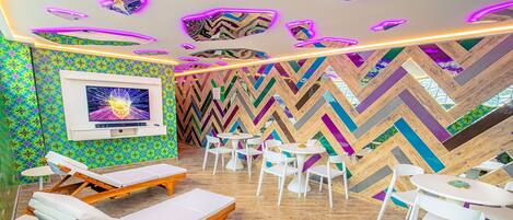 A modern lounge area with wooden flooring, white lounge chairs, and tables.