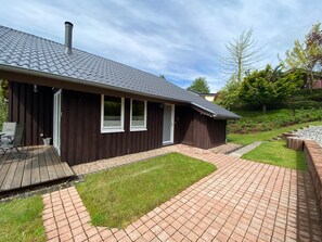 A modern house with a dark brown exterior, a tiled roof, and a paved patio area.