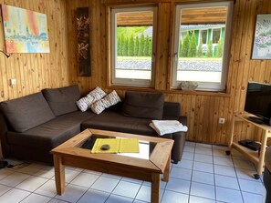 Een kamer met houten lambrisering, een bank, een salontafel en een televisie op een standaard.