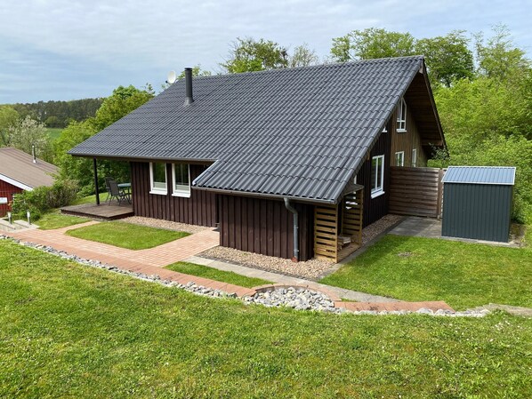 A two-story house with a sloped roof, a covered porch, and a small shed.