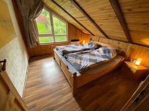 A cozy attic bedroom with a wooden bed, a window with curtains, and a nightstand with a lamp.
