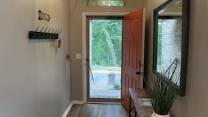Un couloir avec un plancher en bois, un porte-manteau, une plante en pot et une porte donnant sur l’extérieur.