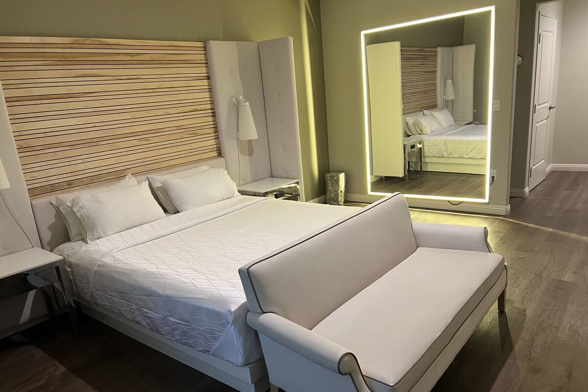 A modern bedroom with a large bed, a bedside table, a nightstand, a mirror, and a bench.