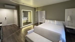 A modern hotel room with a large bed, a seating area, a mirror, and a wardrobe. - Aspire Inn & Suites Orange (Orange)