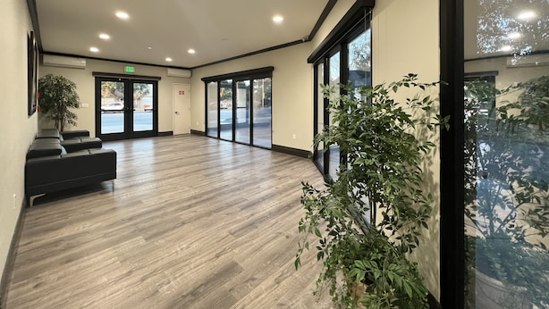 A spacious lobby with a wooden floor, a reception desk, and large glass doors leading outside. - Aspire Inn & Suites Orange (Orange)
