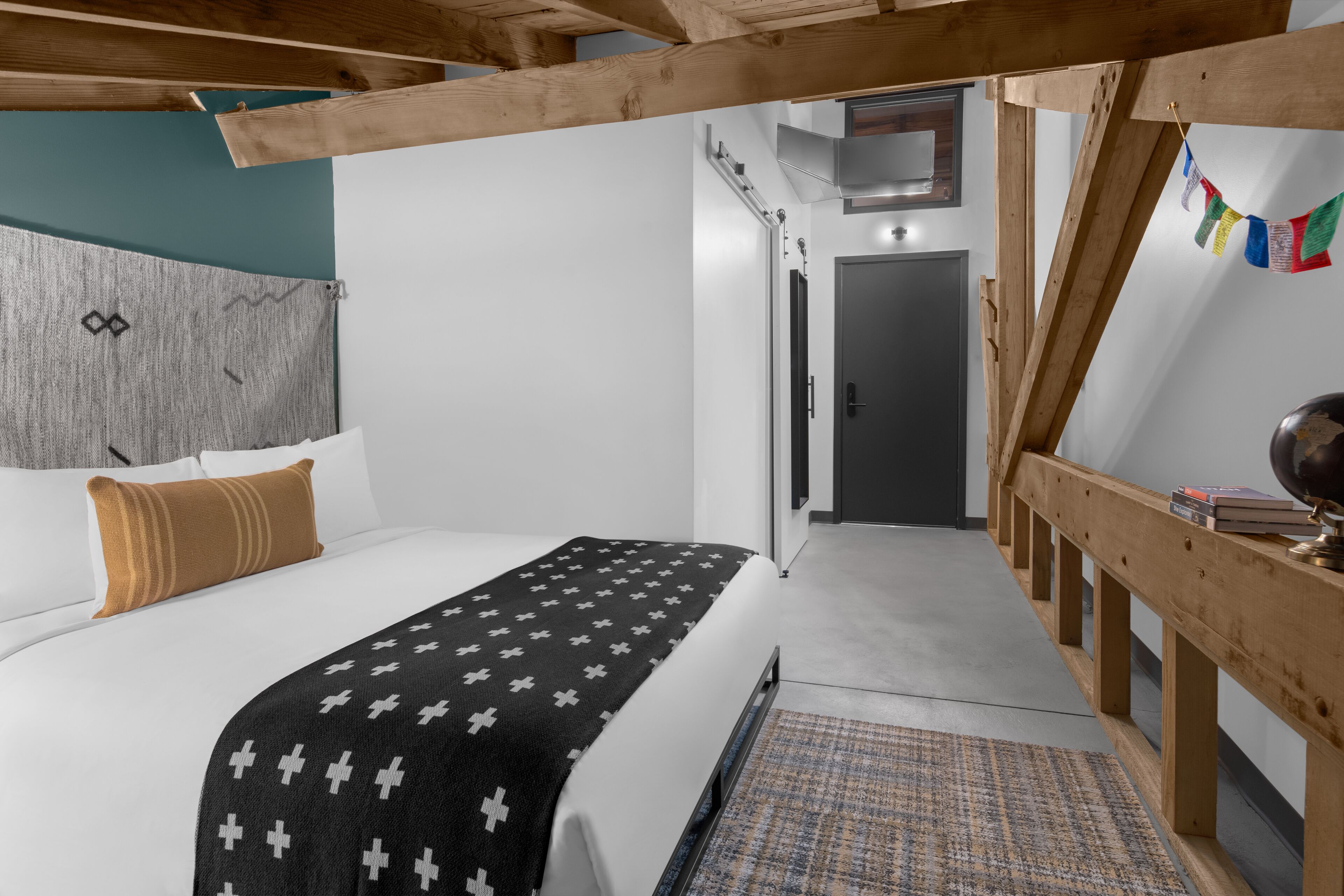 Een slaapkamer met een bed, een houten hoofdeinde, een geborduurd dekbed, een klein vloerkleed en een houten bankje.