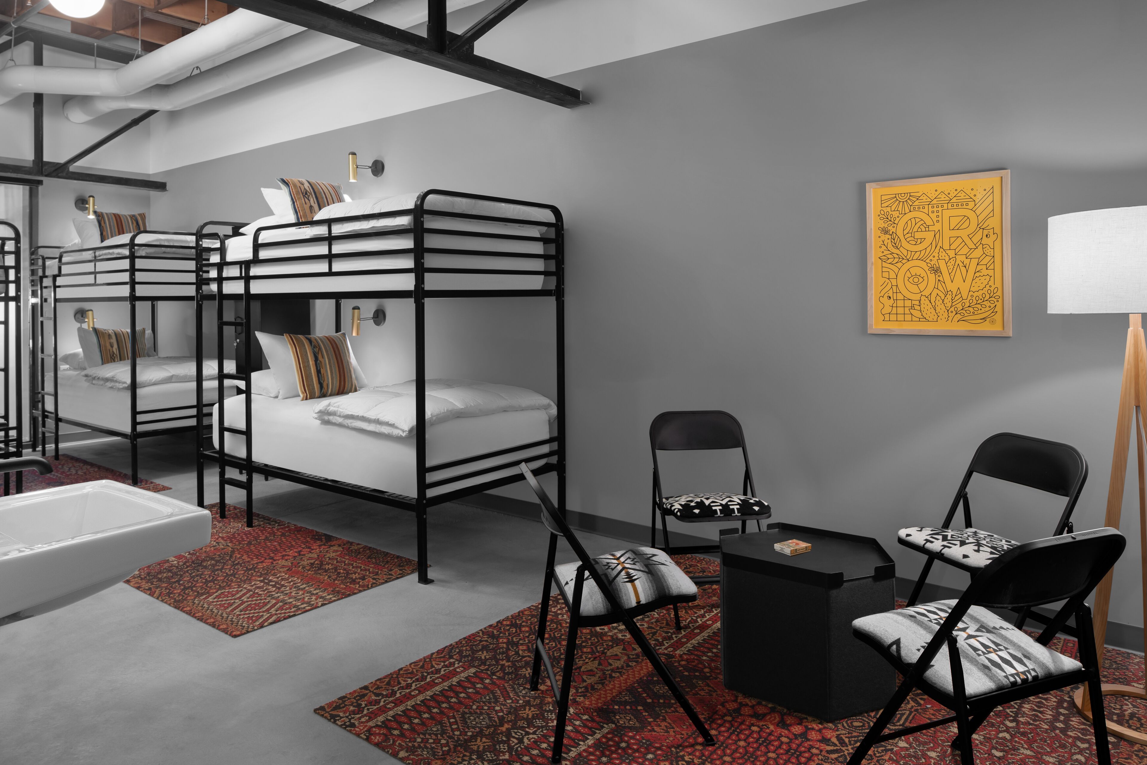 A modern, compact hotel room with bunk beds, a small desk, a chair, and a bedside table.