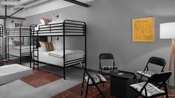 Une chambre d’hôtel moderne et compacte, équipée de lits superposés, d’un petit bureau, d’une chaise et d’une table de chevet.