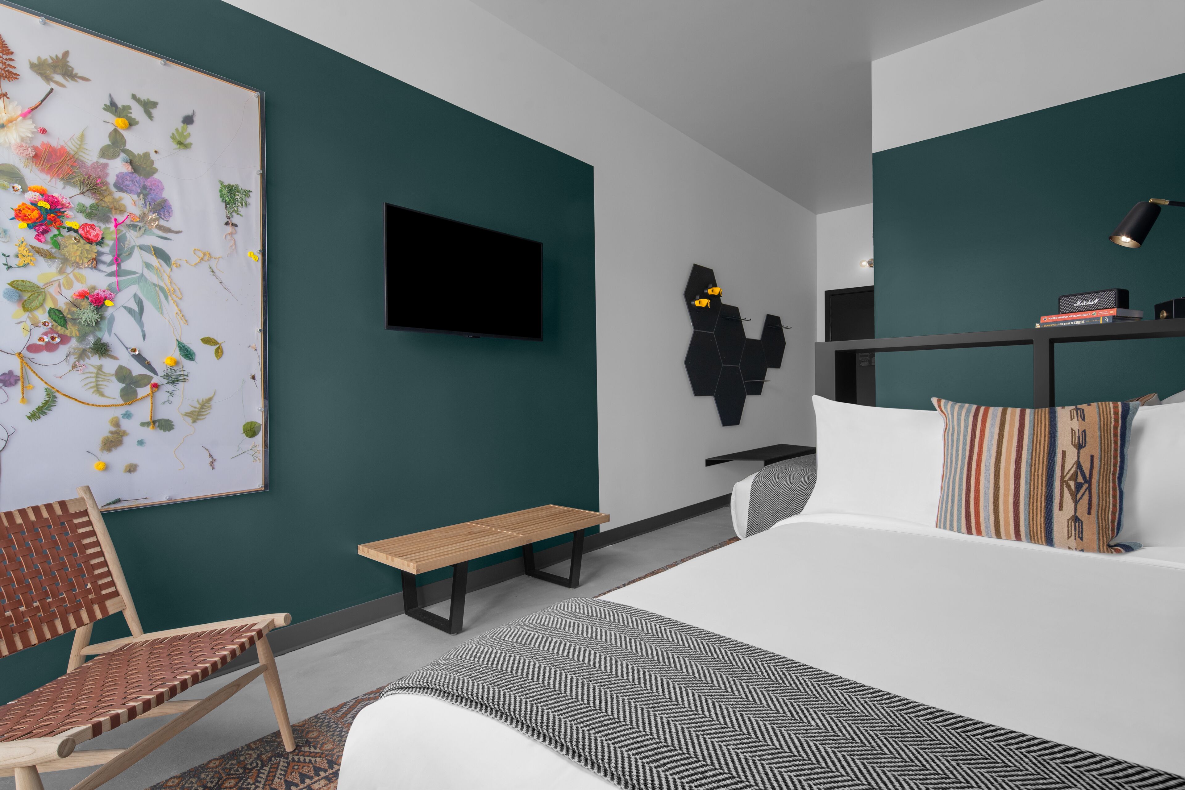 A modern bedroom with a bed, a desk, a chair, a TV, and a wall art piece.