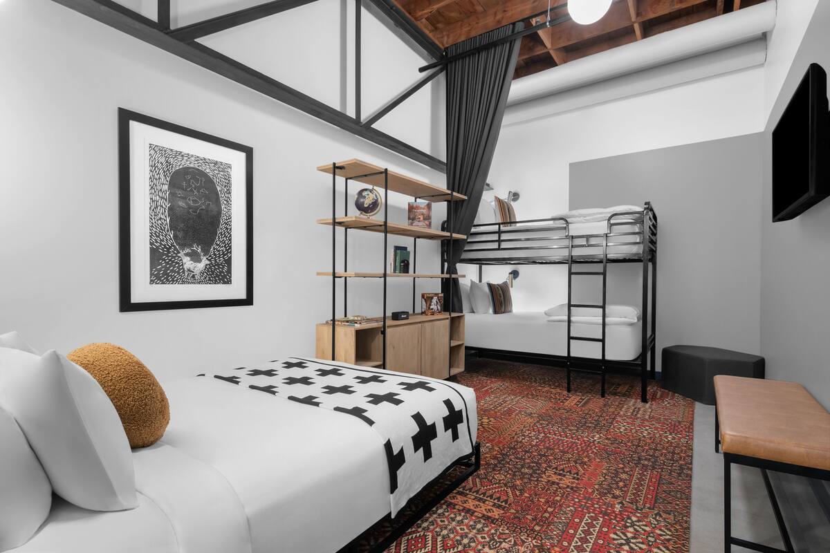 A modern, compact bedroom with a bunk bed, a white sofa, a patterned rug, and a framed artwork on the wall.