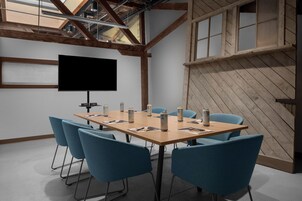 Una sala de conferencias con una mesa grande, sillas azules, un televisor de pantalla plana y vigas de madera.
