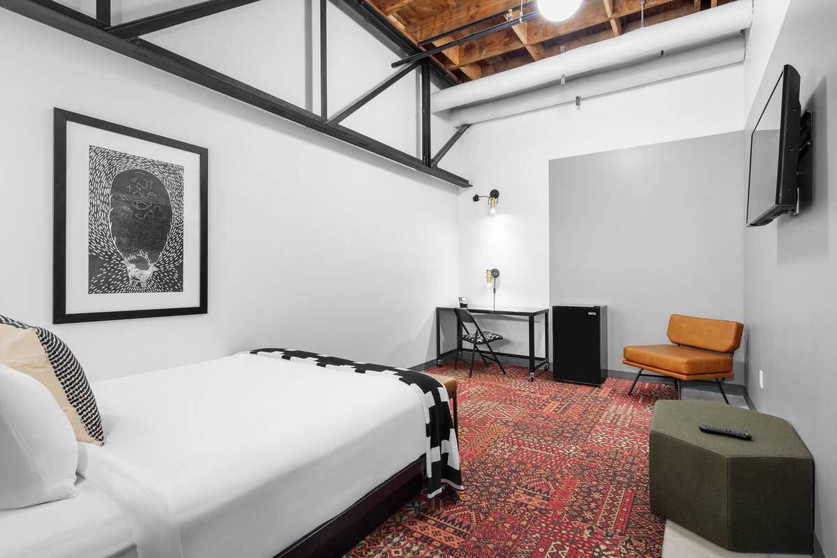 A modern hotel room with a bed, desk, chair, and a TV mounted on the wall.