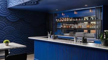 A bar area with a blue and white color scheme, featuring a bar counter, shelves with bottles, and a seating area with a table and chairs.