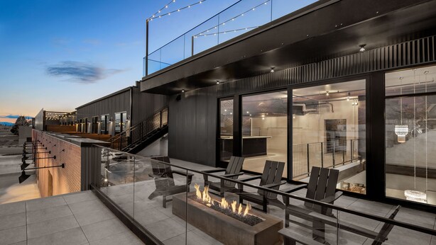 Un espacio moderno al aire libre con área de estar, chimenea, barandillas de vidrio y vista del interior.