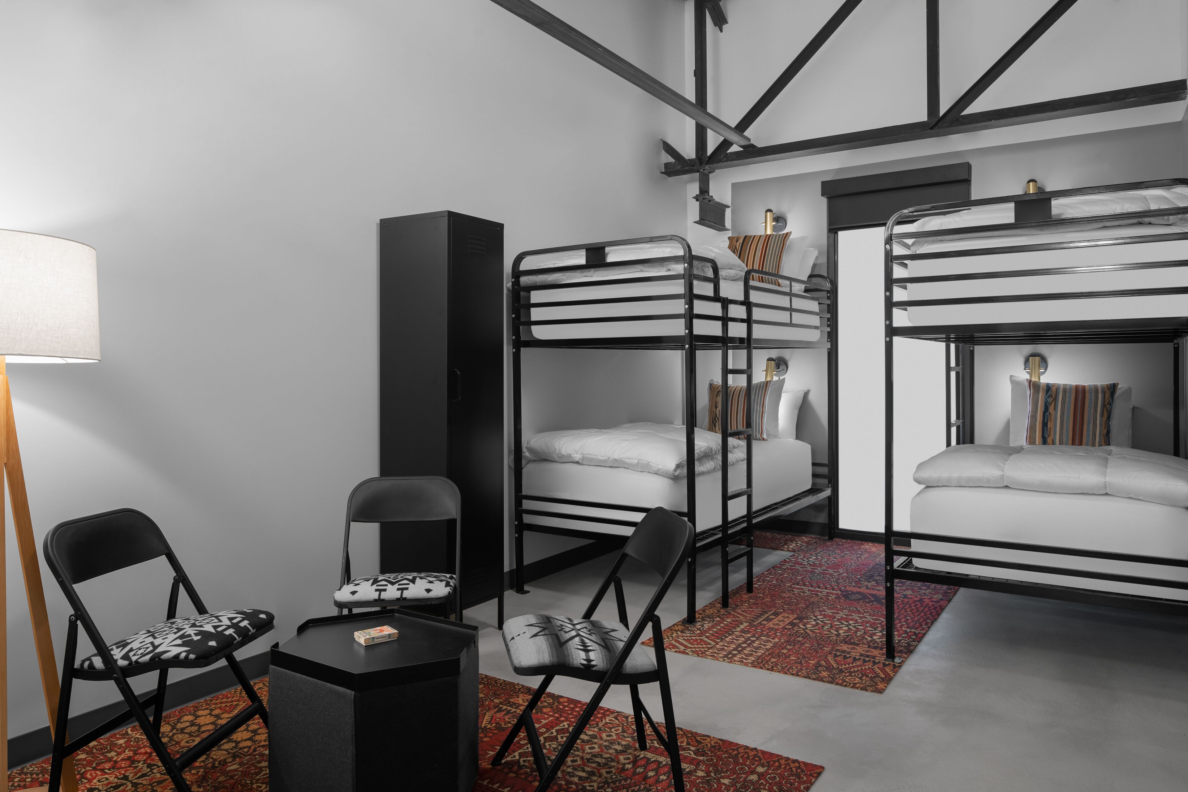 A bunk bed room with a desk, chairs, and a lamp.