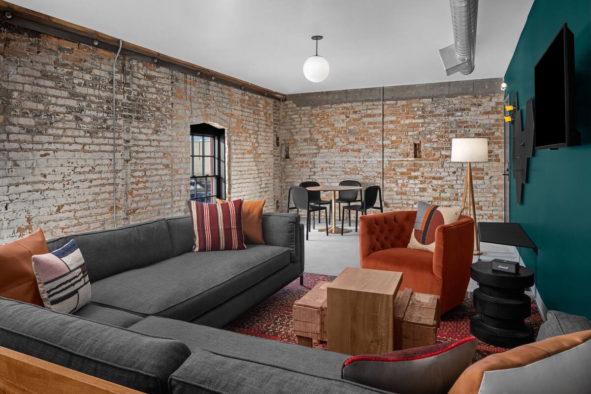 A modern living room with a brick wall, grey sofas, a wooden coffee table, and a teal accent wall.