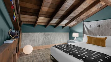 Una camera da letto con soffitto in legno, un letto con coperta a motivi decorativi, un comodino con lampada e un globo su uno scaffale.