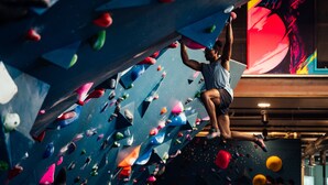 Una persona escalando una pared de roca multicolor con diferentes puntos de agarre y apoyo.