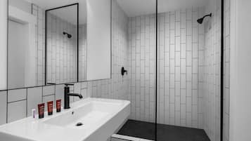 Un baño moderno con un lavamanos blanco, grifo negro y ducha con mampara de vidrio.