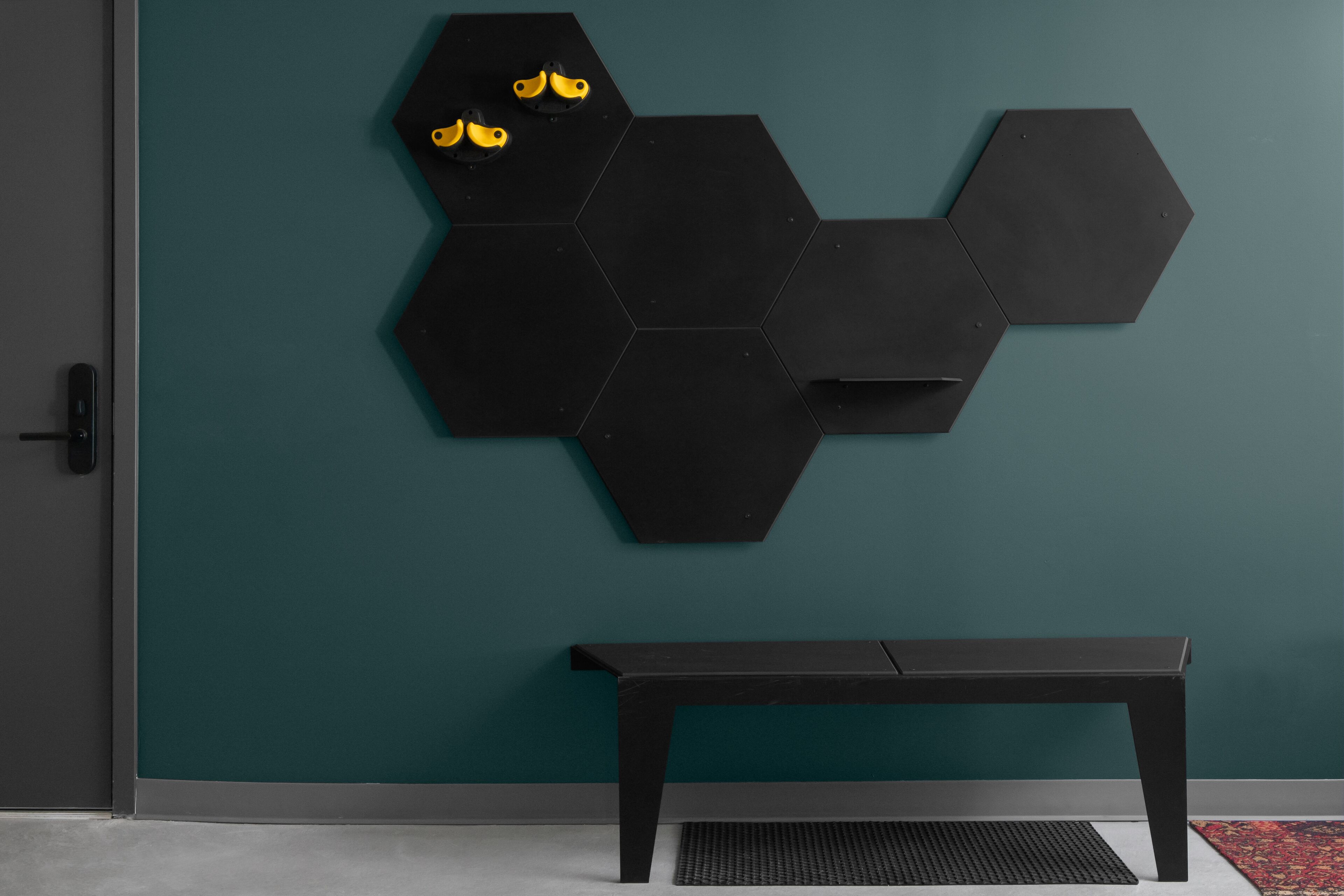A room with teal walls, a black hexagonal wall art piece, and a black bench.