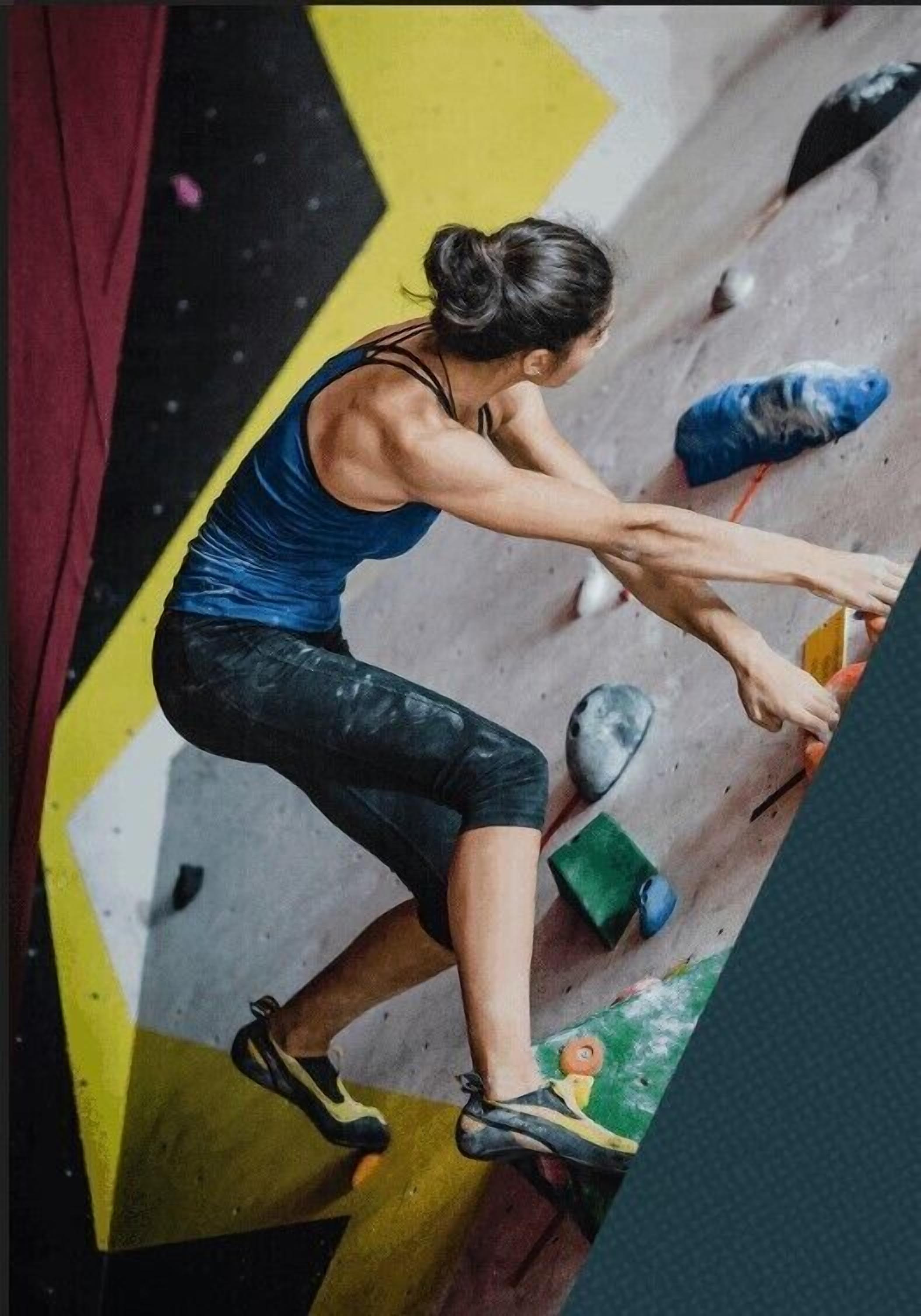 A person climbing a rock wall with various colored holds.
