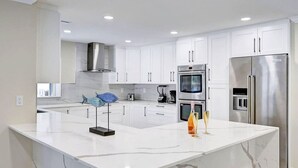 A modern kitchen with white cabinets, stainless steel appliances, and a marble island. - Luxury 5BR/3BA Villa Walk to  Hollywood Beach (Hollywood)