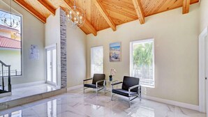 A spacious room with a high wooden ceiling, a marble floor, two chairs, a small table with a vase, and large windows with blinds. - Luxury 5BR/3BA Villa Walk to  Hollywood Beach (Hollywood)