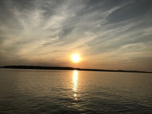 A sunset over a calm body of water with a distant shoreline. - 3 bedroom/2 full bath lakefront home with gentle slope to private covered dock (Cadiz)