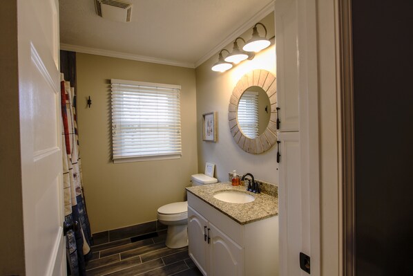 A bathroom with a toilet, sink, and vanity. There are blinds on the window, and a mirror above the sink.