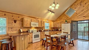 A wooden cabin-style kitchen with a central island, bar stools, and a dining table. - Cabin with hot tub firepit fireplace and game room area!near Helen  (Sautee Nacoochee)