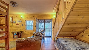 A cozy cabin interior with a wooden interior, a leather sofa, a bed, and a small desk with a computer. - Cabin with hot tub firepit fireplace and game room area!near Helen  (Sautee Nacoochee)