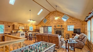 A cozy log cabin interior with a dining area, kitchen, living room, and a foosball table. - Cabin with hot tub firepit fireplace and game room area!near Helen  (Sautee Nacoochee)