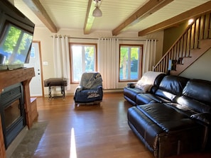 A living room with a fireplace, a leather sofa, a covered armchair, and a staircase. - Cozy house with spa 10 minutes from Village Vacances Valcartier. (Saint-Gabriel-de-Valcartier)