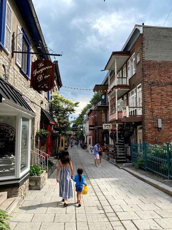 A street with buildings, a sign reading 'Le Forgeron D'ore,' and a person walking with a child.
