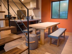 A modern kitchen with a central island, wooden staircase, and a dining area with a bench.