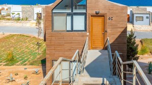 Un bâtiment moderne avec une façade en bois, un escalier menant à une porte marquée « 4C », et une vue sur la mer en arrière-plan.