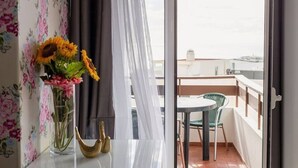 Ein Balkon mit Tisch und Stühlen, einer Blumenvase und Blick auf ein Gewässer sowie Gebäude.