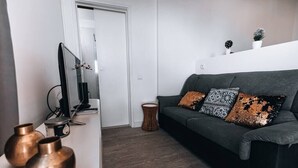 Ein modernes Wohnzimmer mit einem grauen Sofa, dekorativen Kissen und zwei Kupfervasen auf einer weißen Oberfläche.