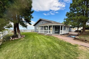 A single-story house with a porch, surrounded by a white fence and a grassy yard. - FARMHOUSE W/MOUNTAIN VIEWS! (Parker)